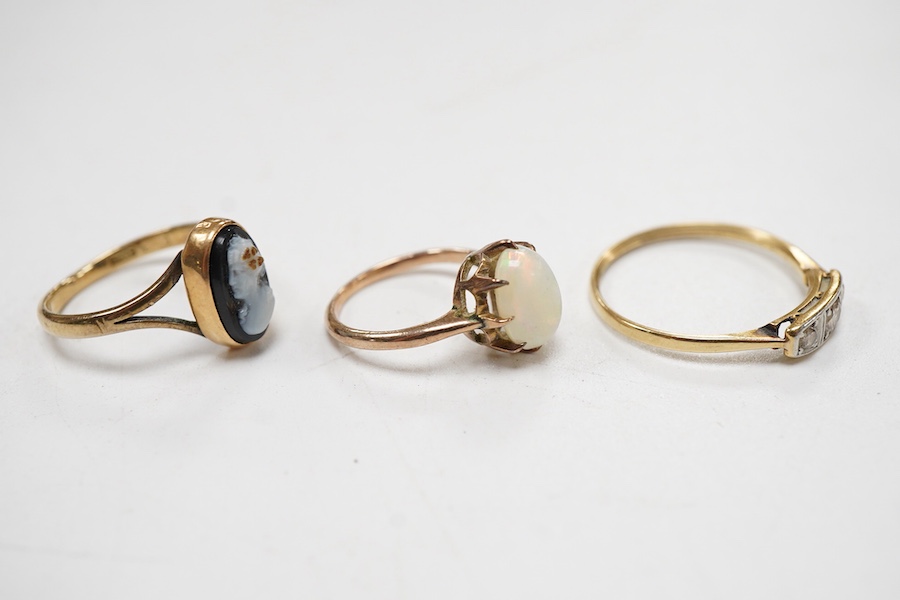 A group of rings to include a three stone diamond 18ct ring, size P, a hardstone cameo 9ct ring, size K and an opal set yellow metal ring, size D.
